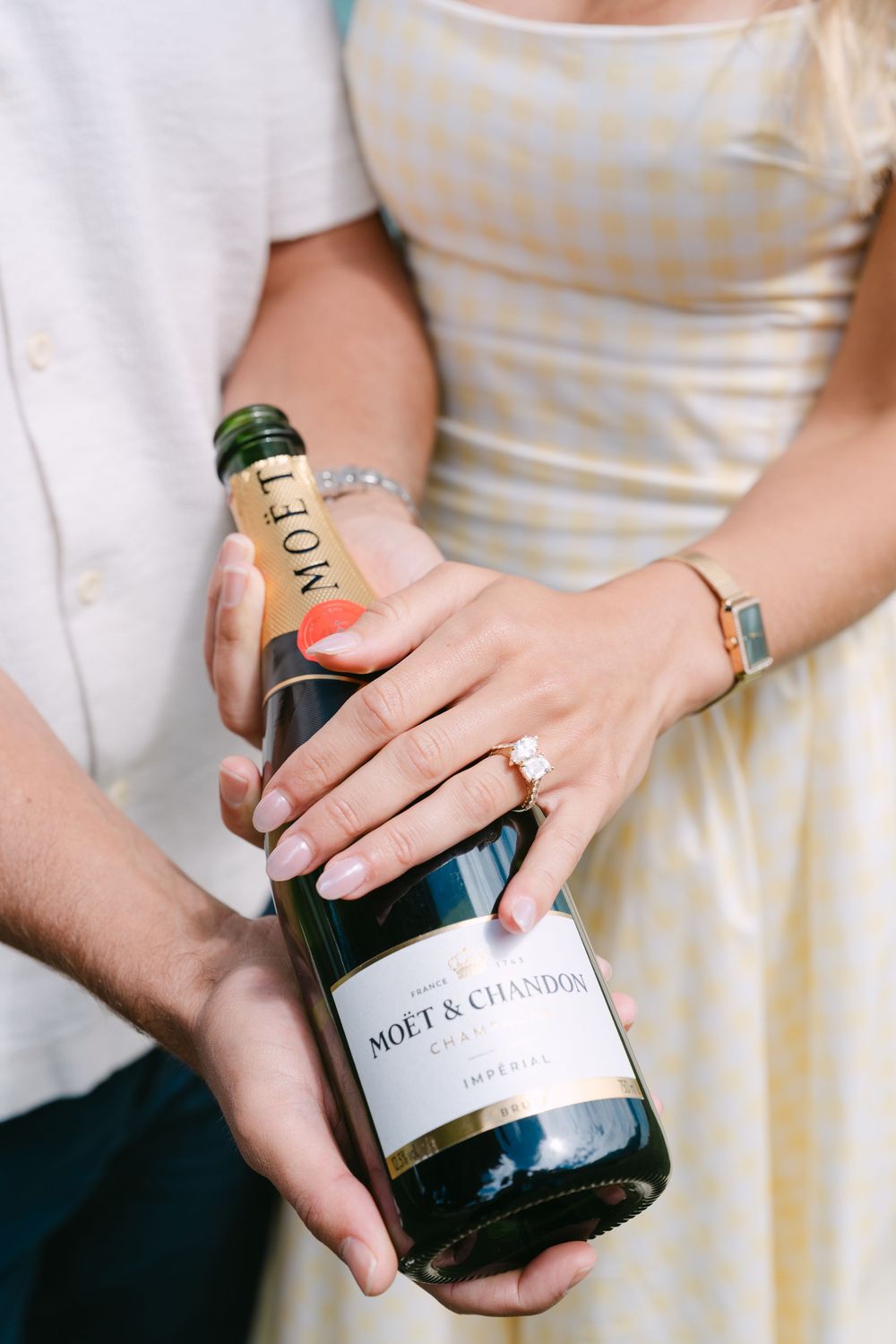 Couple holding a Moet & Chandon Champagne bottle, woman wearing an engagement ring and gold watch.