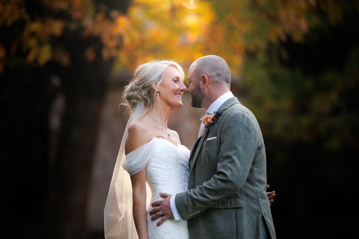 Bride and groom share a romantic moment outdoors, surrounded by golden autumn foliage in a stunning wedding portrait.