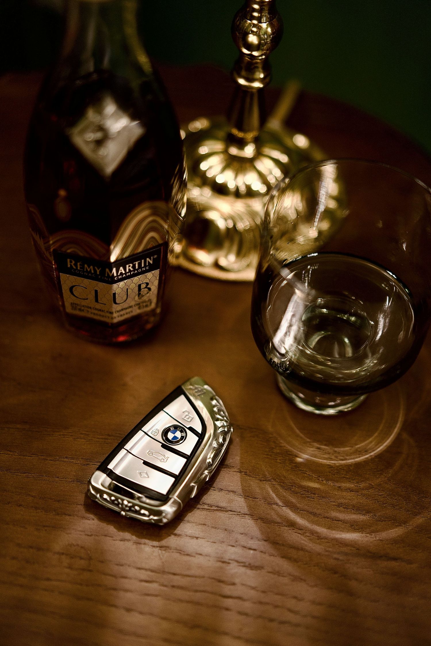 BMW car key beside a glass of Remy Martin Club cognac on a wooden table, suggesting luxury lifestyle.