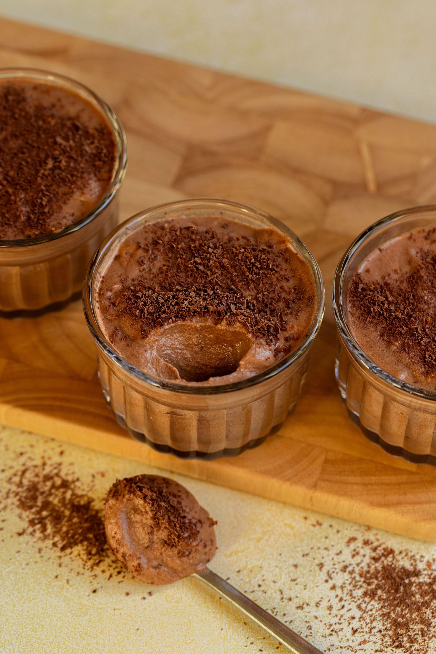 A spoon scoops creamy chocolate mousse from a glass bowl showing its smooth and airy texture.