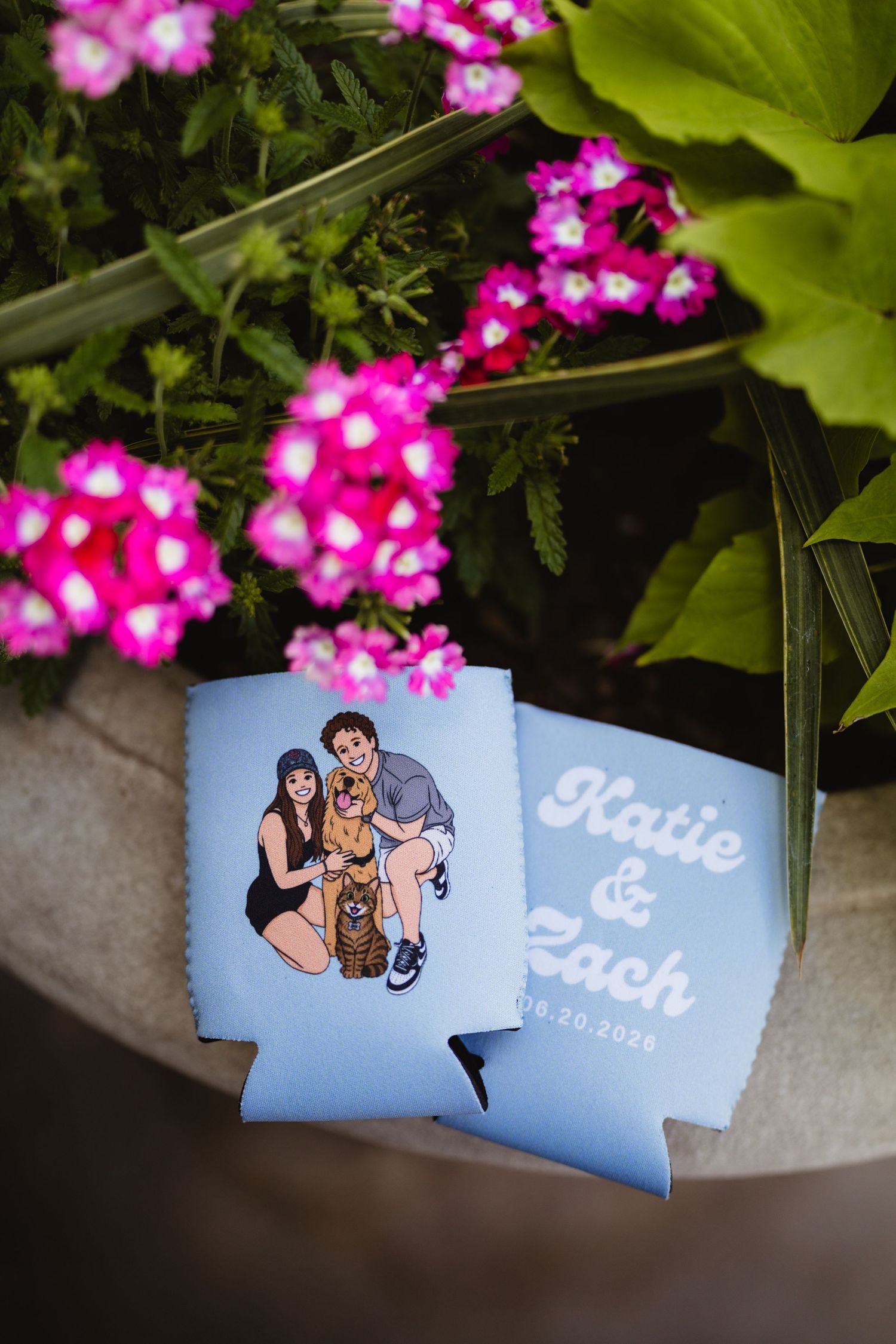 Custom blue wedding koozies for Katie & Zach dated 06.20.2025, featuring a couple portrait with pet, surrounded by pink flowers.