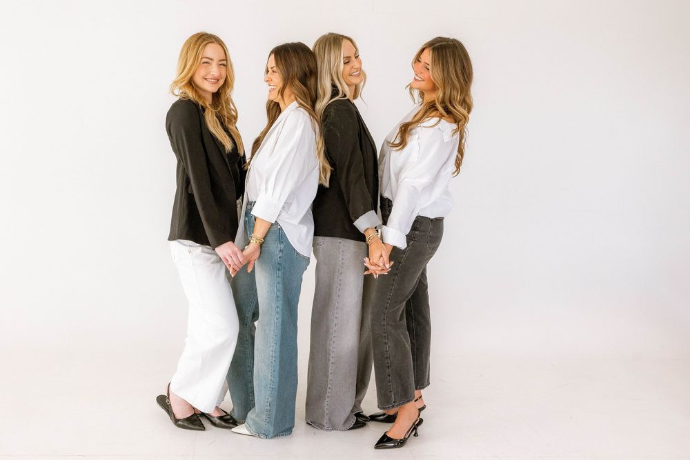 Four women in black and white outfits pose together against a white background in a stylish group photo.