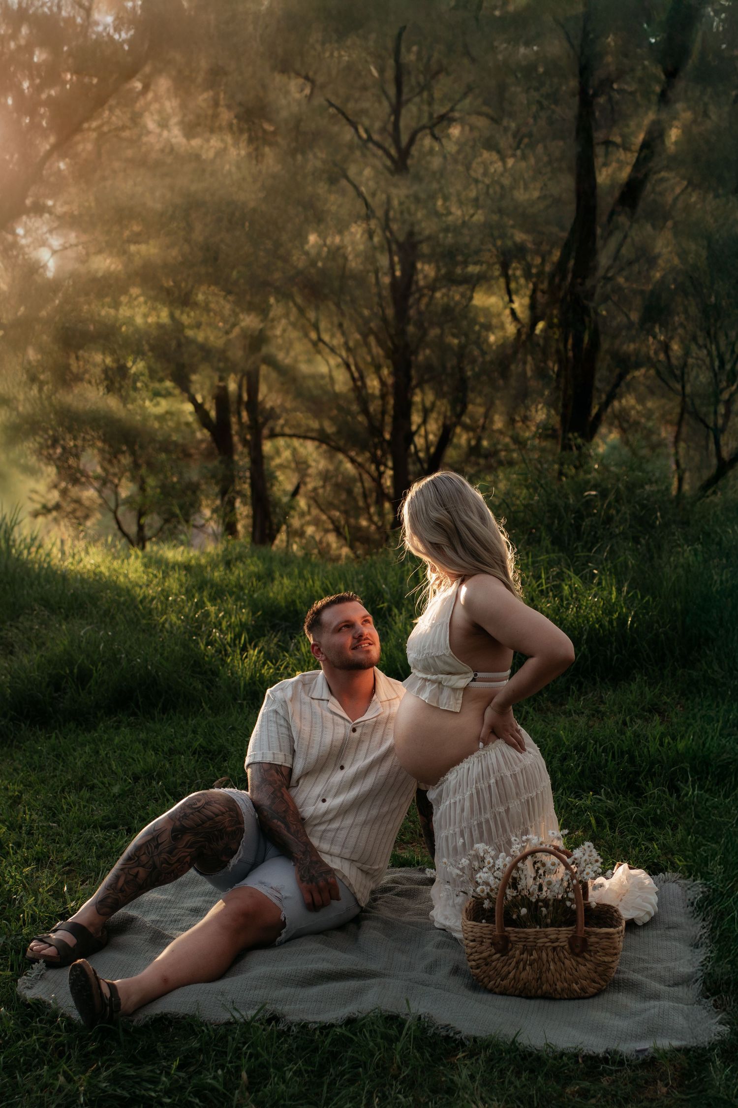 Pregnant couple at sunset in a Penrith wooded location with the filtered sun coming through the trees