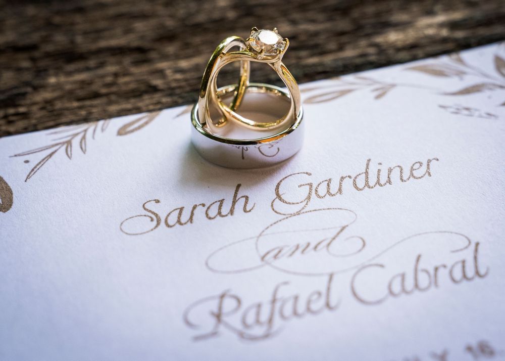 Gold wedding rings resting on a wedding invitation for Sarah Gardiner and Rafael Cabral.