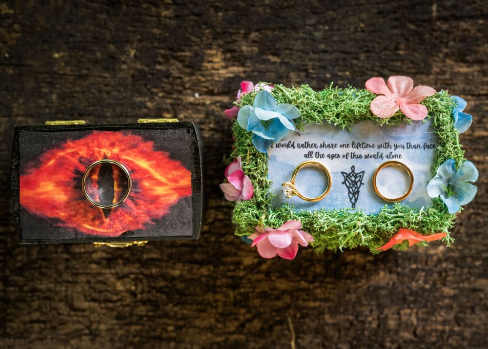 Lord of the Rings themed wedding ring boxes with moss, flowers, and the Eye of Sauron design on rustic wood.