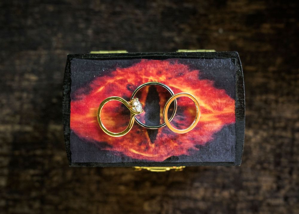 Gold wedding rings resting on a decorative box with fiery Eye of Sauron design on dark wood.