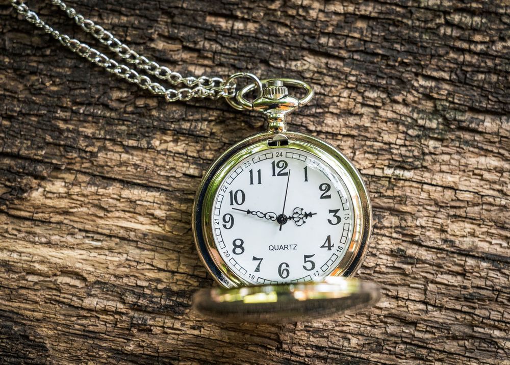 Vintage brass quartz pocket watch with chain resting on rustic wooden surface.