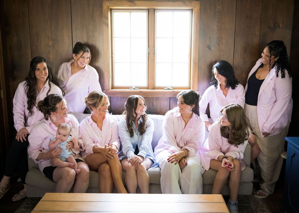 Bridesmaids in pink robes gathered together on a couch before a wedding ceremony.