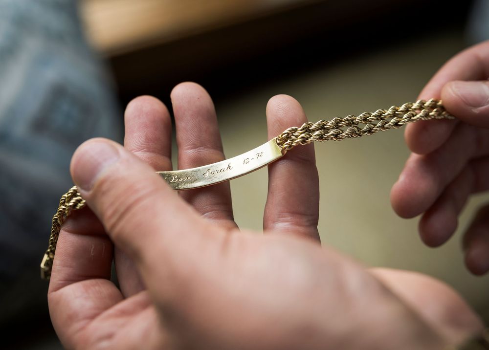 Close-up of hands holding a gold engraved ID bracelet with rope chain detailing.