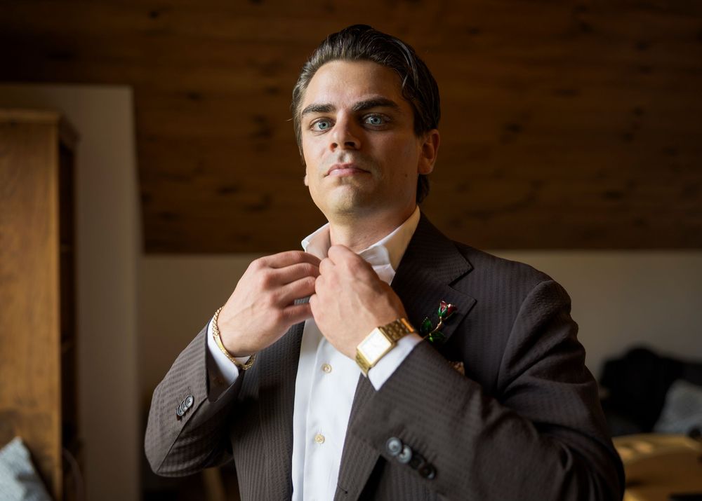 Groom in pinstripe suit adjusting his tie while getting ready for wedding ceremony indoors.