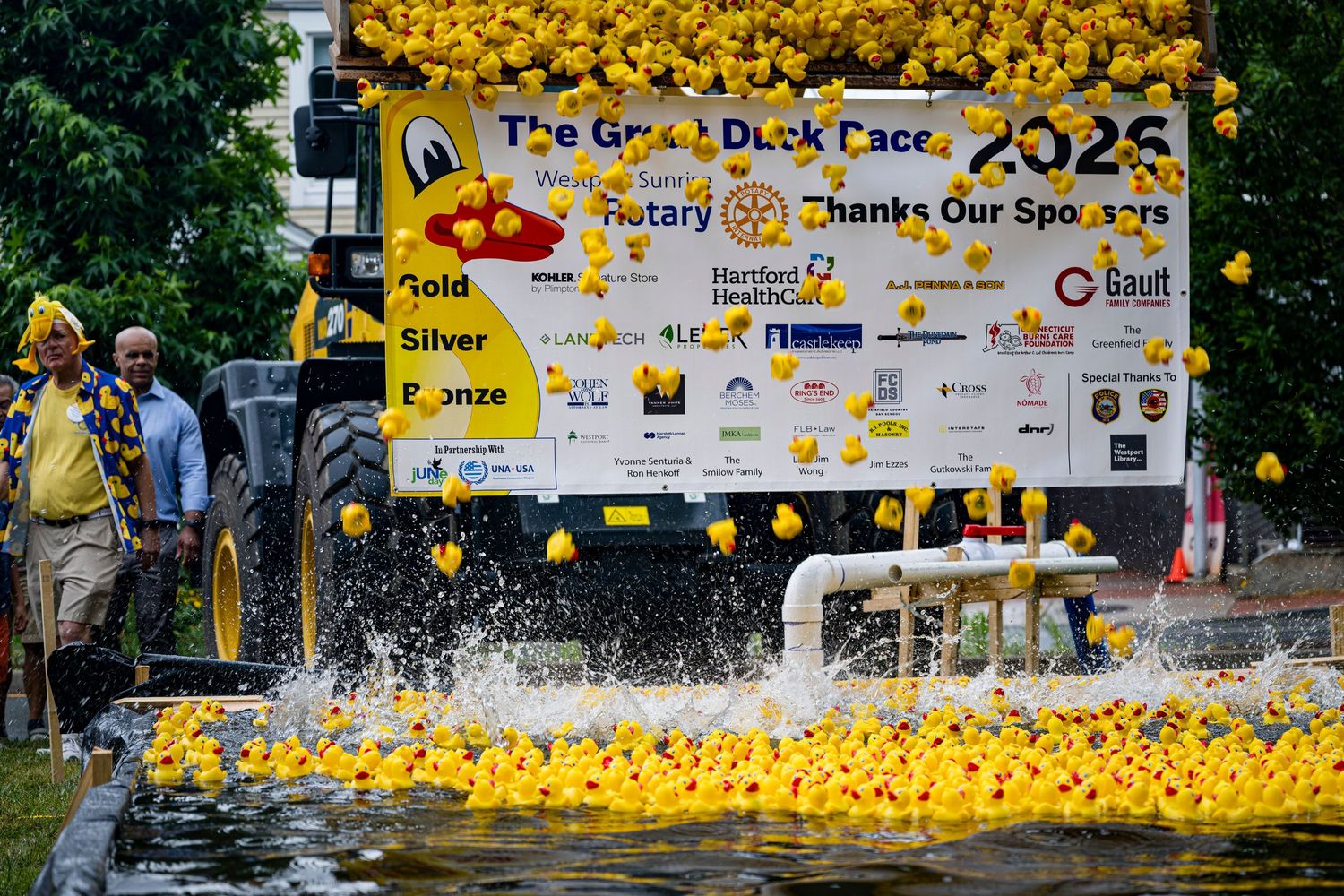 Yellow rubber ducks float in water at the Great Duck Race 2025 Rotary charity event with sponsor banners displayed.