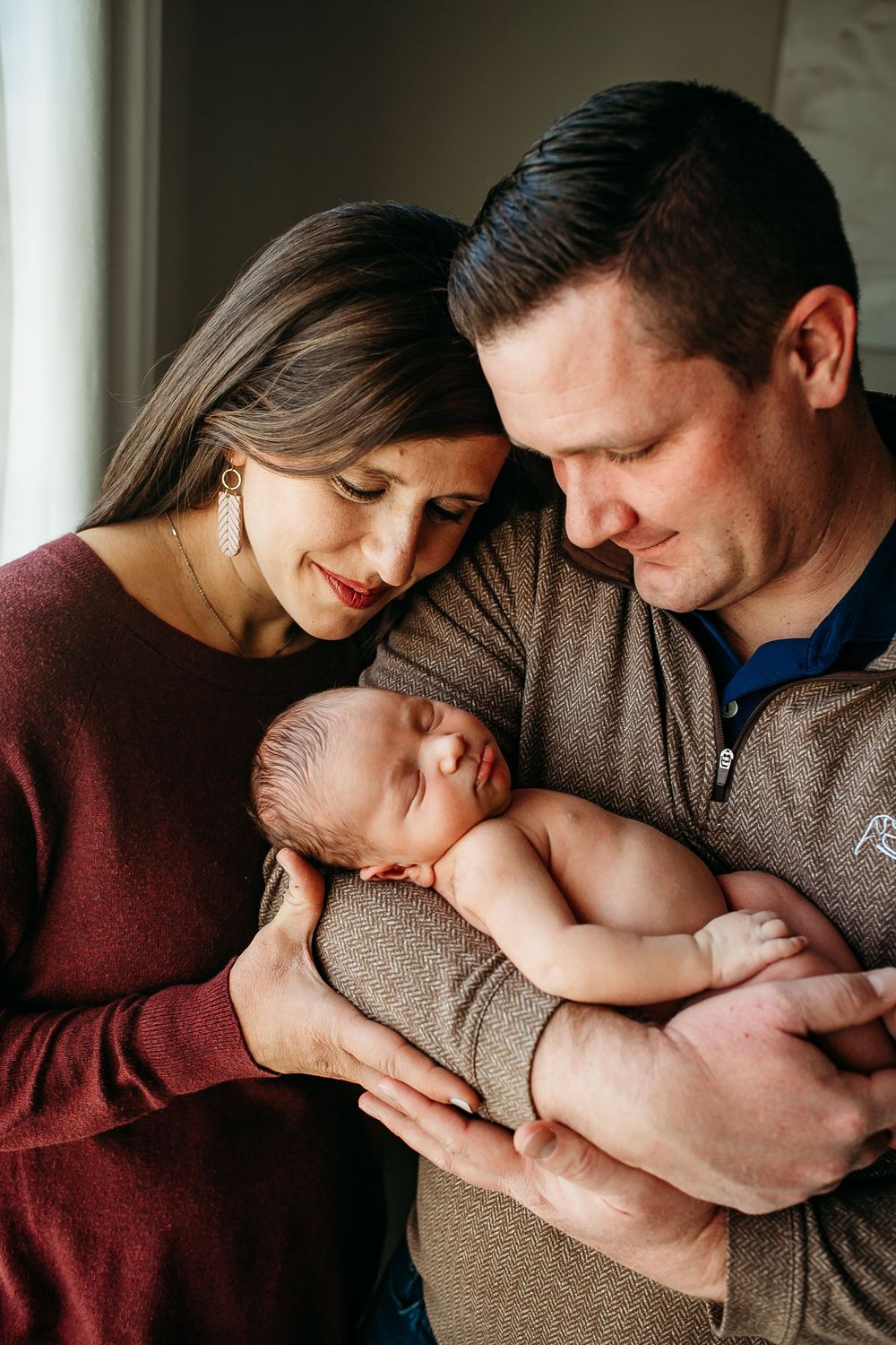 New parents tenderly cradle their sleeping newborn baby together in a warm indoor portrait.