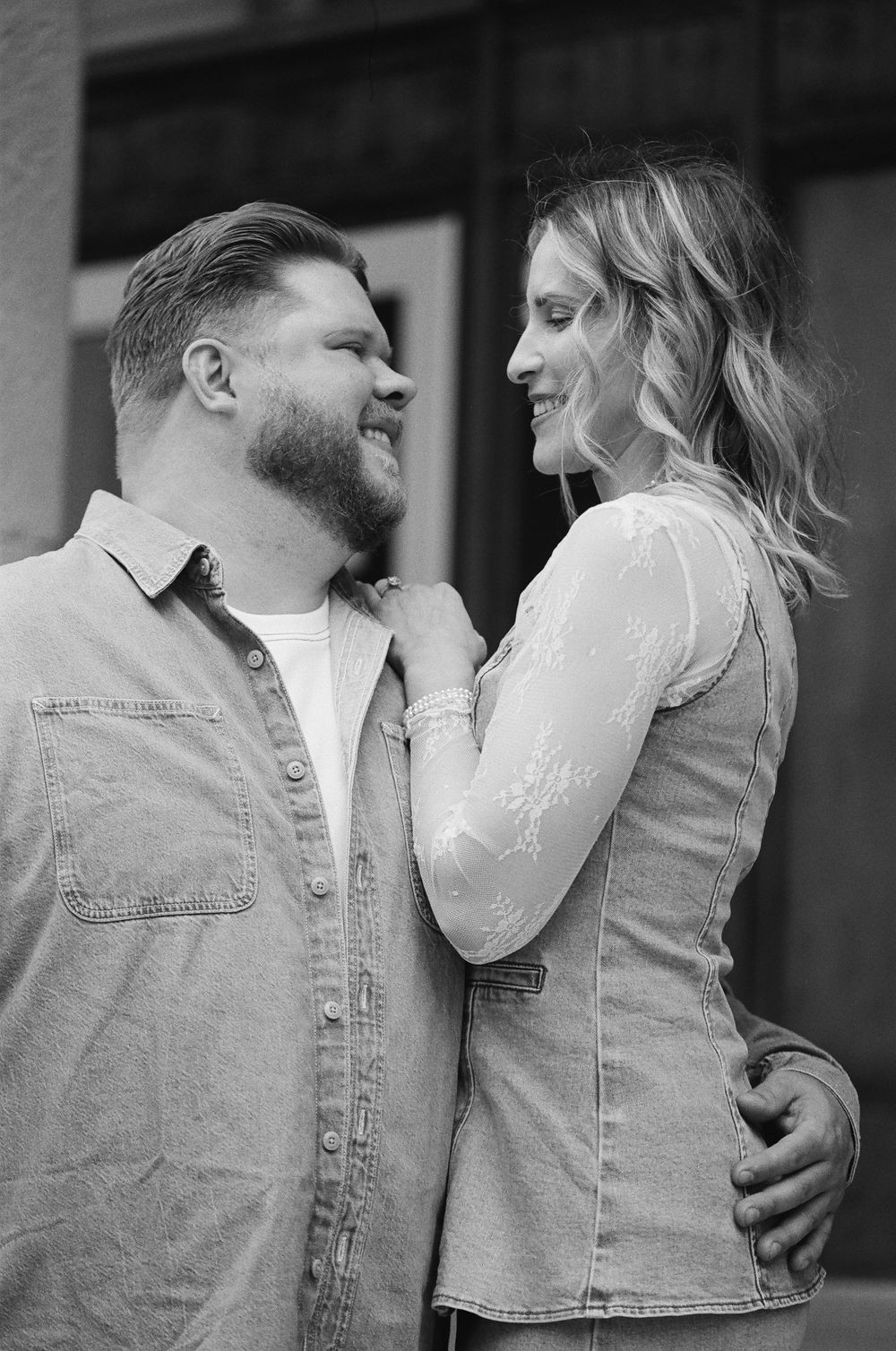 Black and white photo of a smiling couple embracing outdoors, woman placing hand on man's chest.