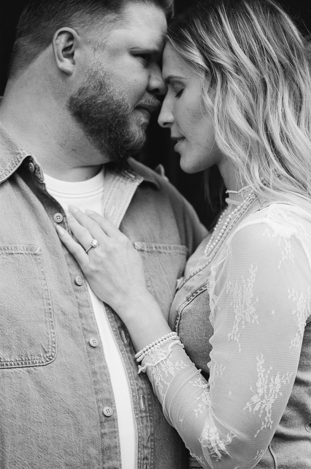 Black and white photo of a romantic couple sharing an intimate moment, the woman wearing a diamond ring and lace dress.