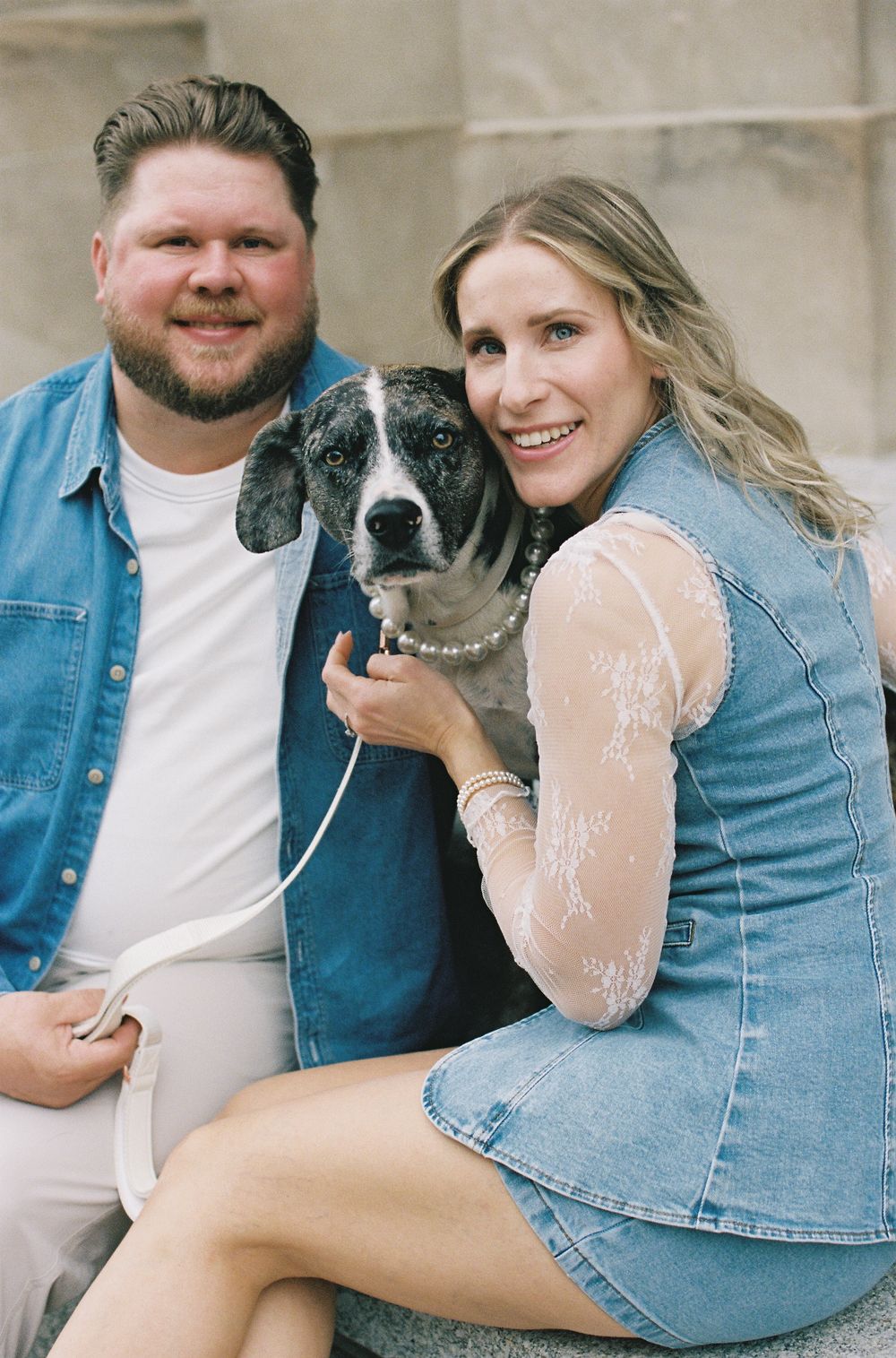 Smiling couple poses with their black and white dog while sitting on stone steps outdoors.