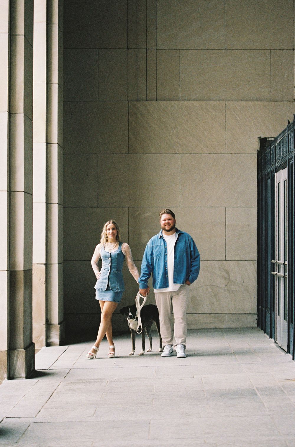 Couple standing with their dog in front of a stone building with tall columns.