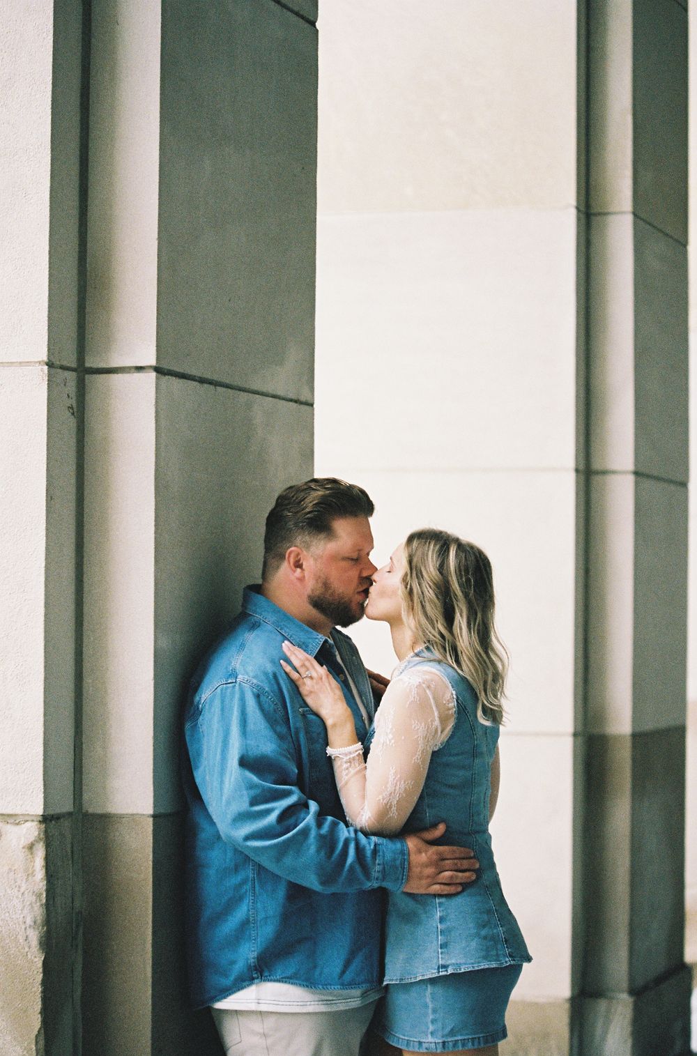 Couple sharing a kiss against stone columns outdoors.