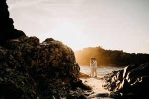 Silhouetted figures walk along rocky coastal cliffs at sunset creating dramatic shadows and golden light.