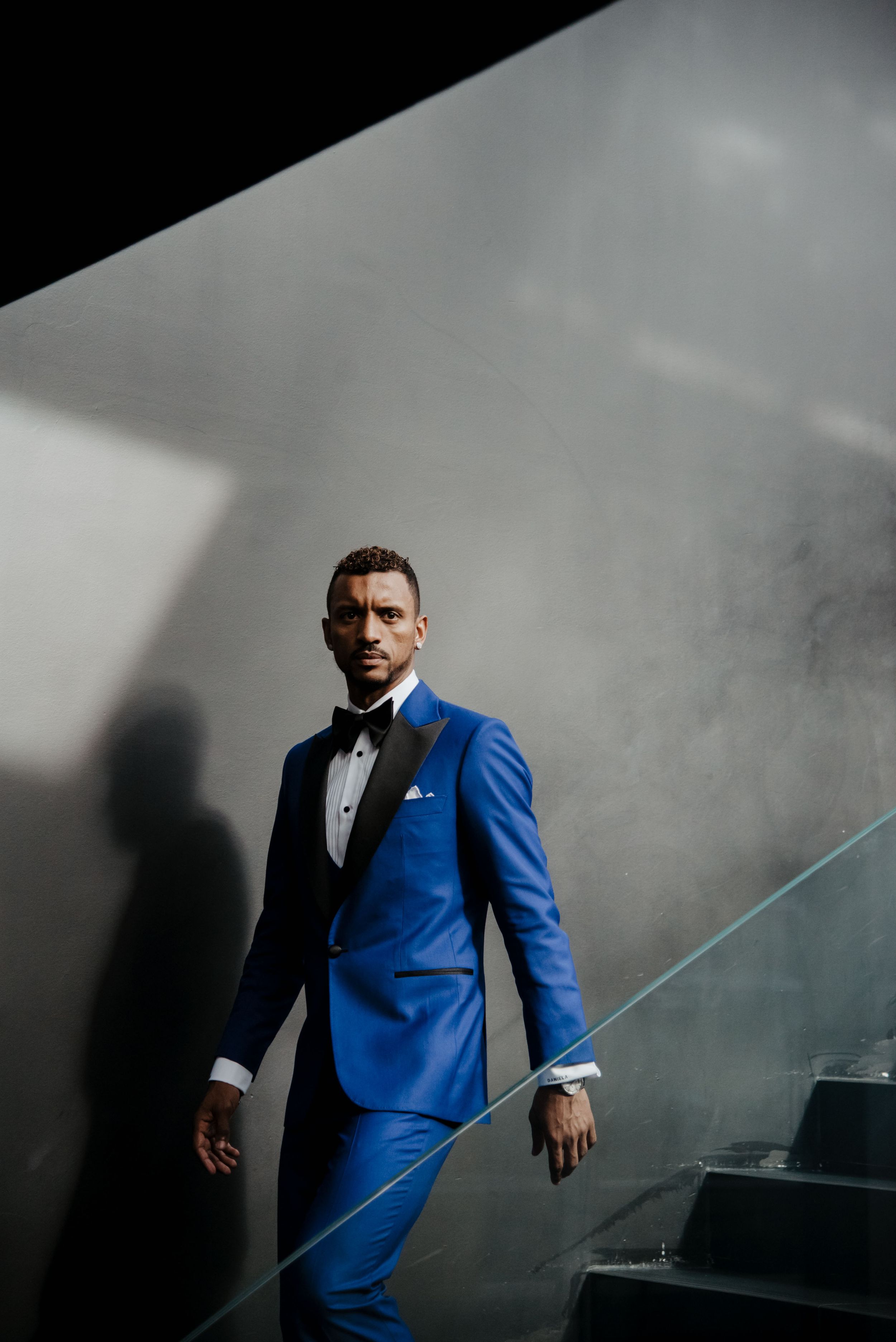 Groom wearing a striking royal blue suit poses dramatically against a moody grey background.