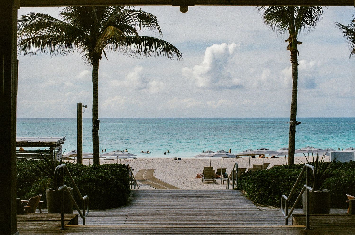 Tropical beach scene with orange umbrellas, white sand, and crystal-clear turquoise water under a blue sky.