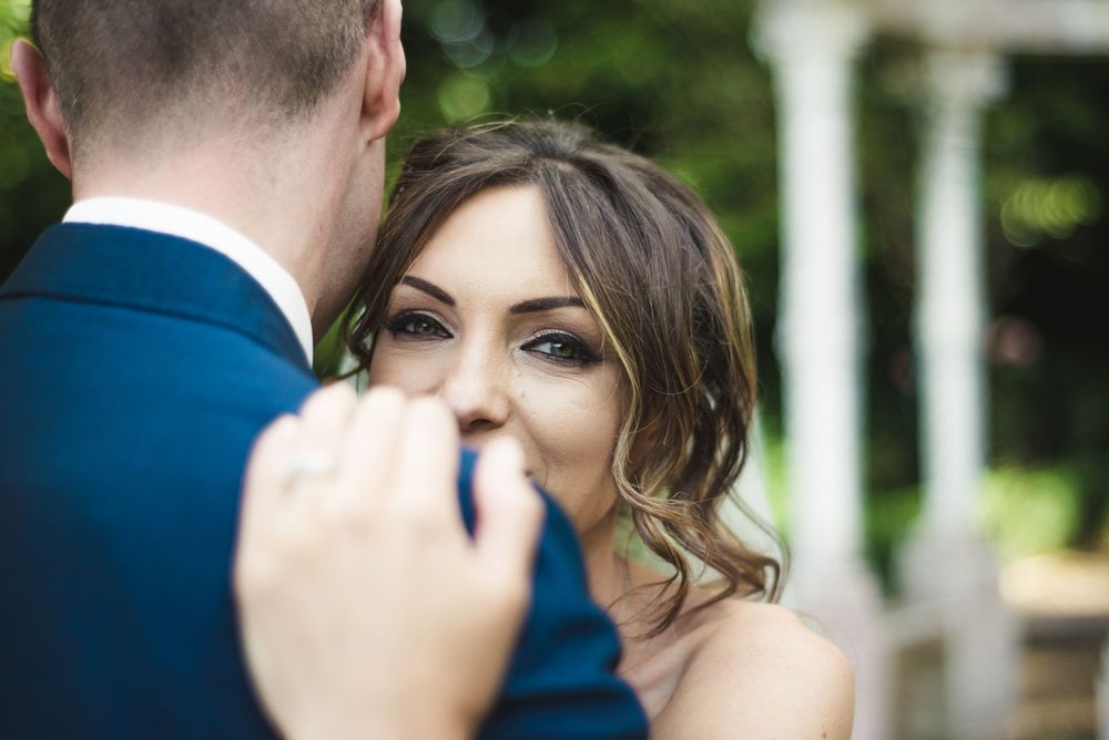 A bride in a blue dress gazes lovingly at her groom during an outdoor wedding ceremony.