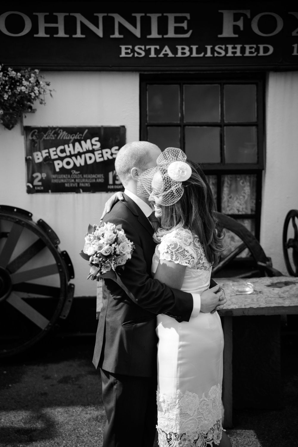 Black and white photo of a bride and groom sharing a kiss outside a vintage Johnnie Fo establishment sign.