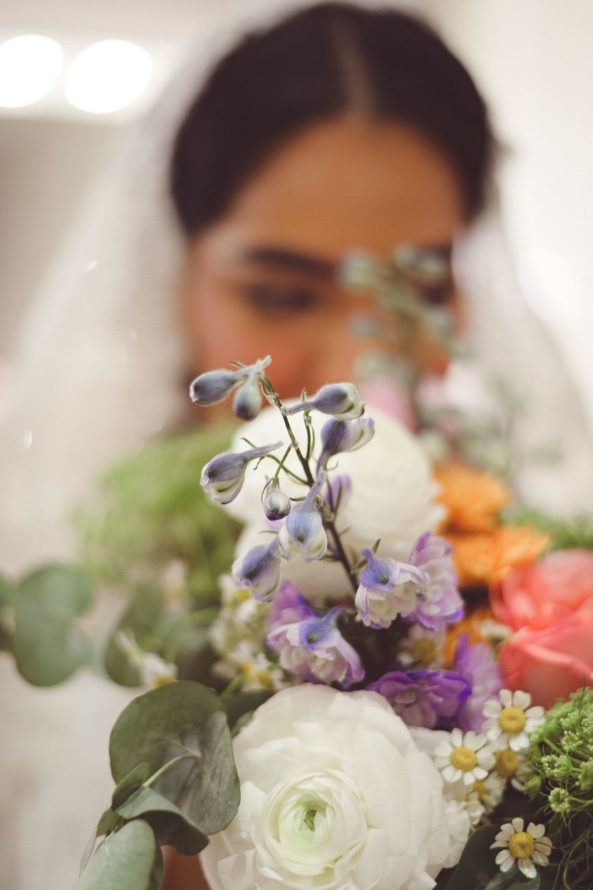 Bride holding a colorful wedding bouquet with white ranunculus, purple flowers, and eucalyptus in soft focus.
