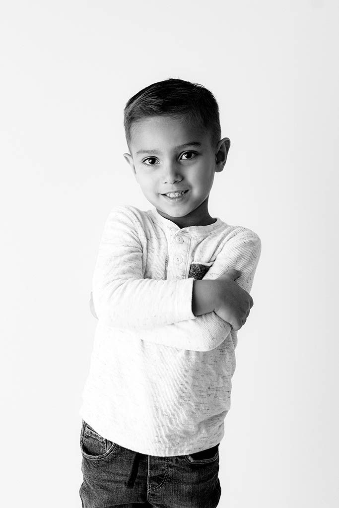 Young boy posing with arms crossed in white long-sleeve shirt and jeans, black and white photo.