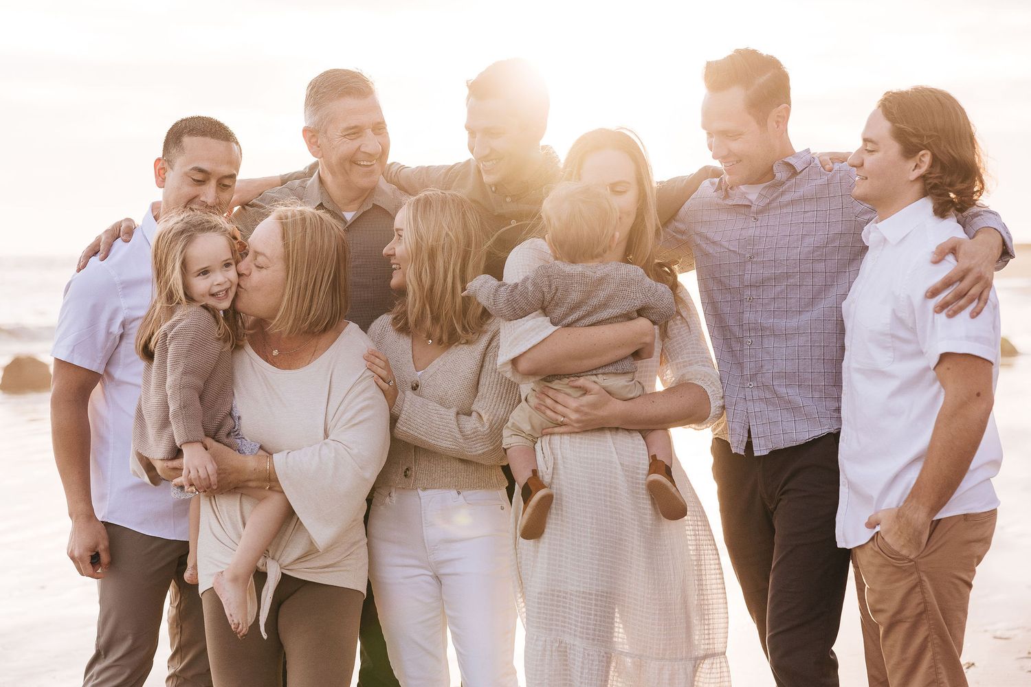 Large family group hugging and smiling together on a sunny beach at golden hour.