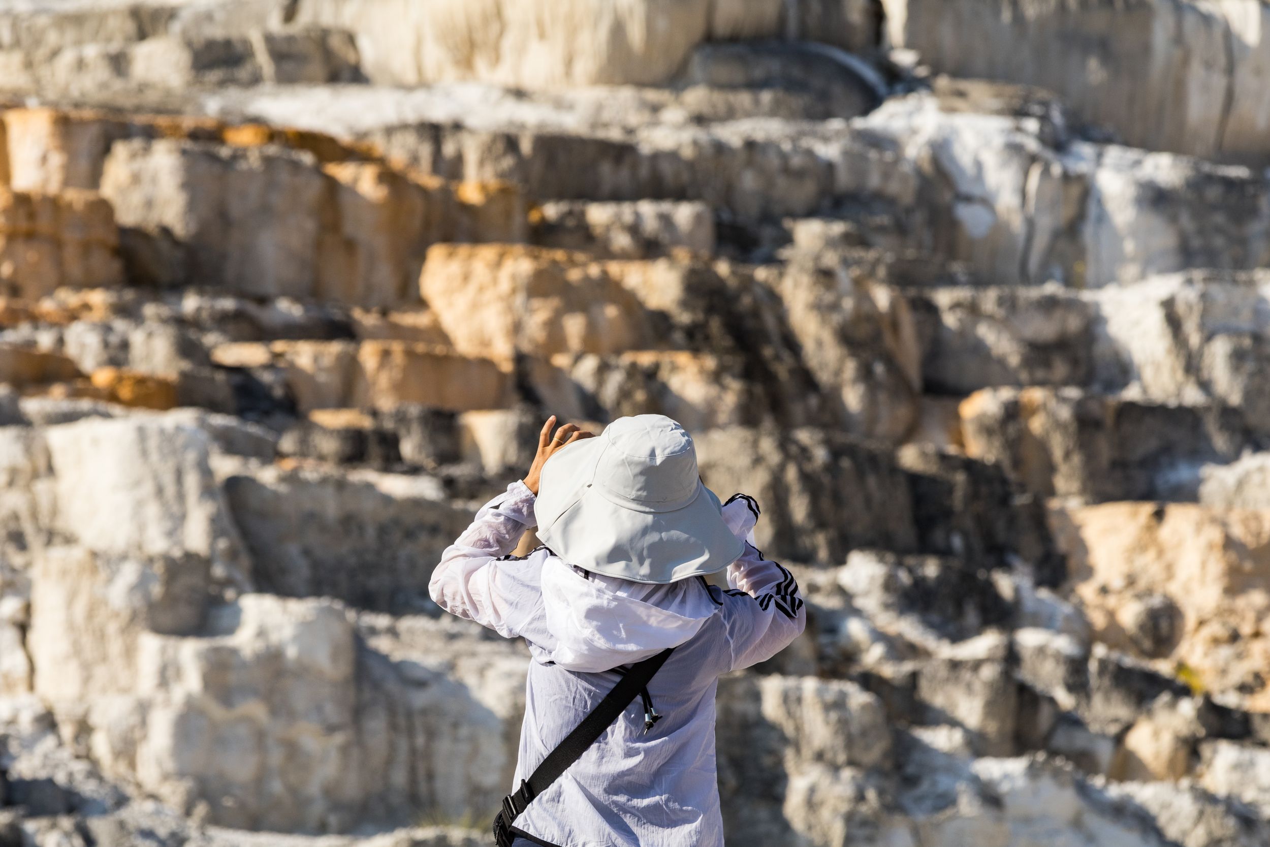 Tourist in hat photographing rocky limestone cliffs formation at scenic outdoor geological landmark.