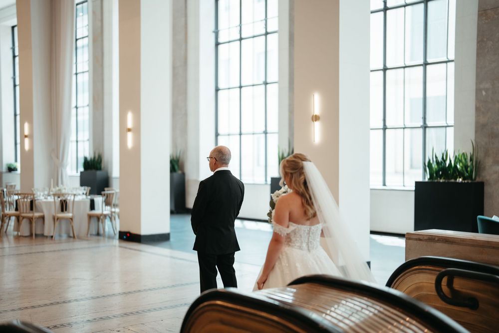 Bride and groom share a romantic moment in an elegant wedding venue with tall windows and modern decor.
