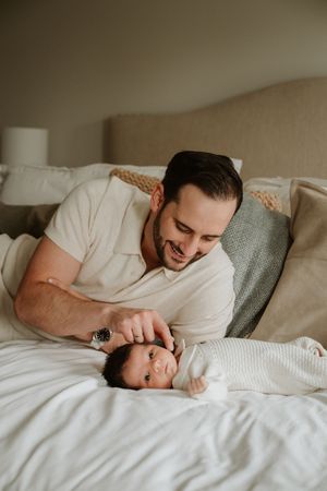Father comforting his newborn baby on the bed during an in-home newborn photography session.