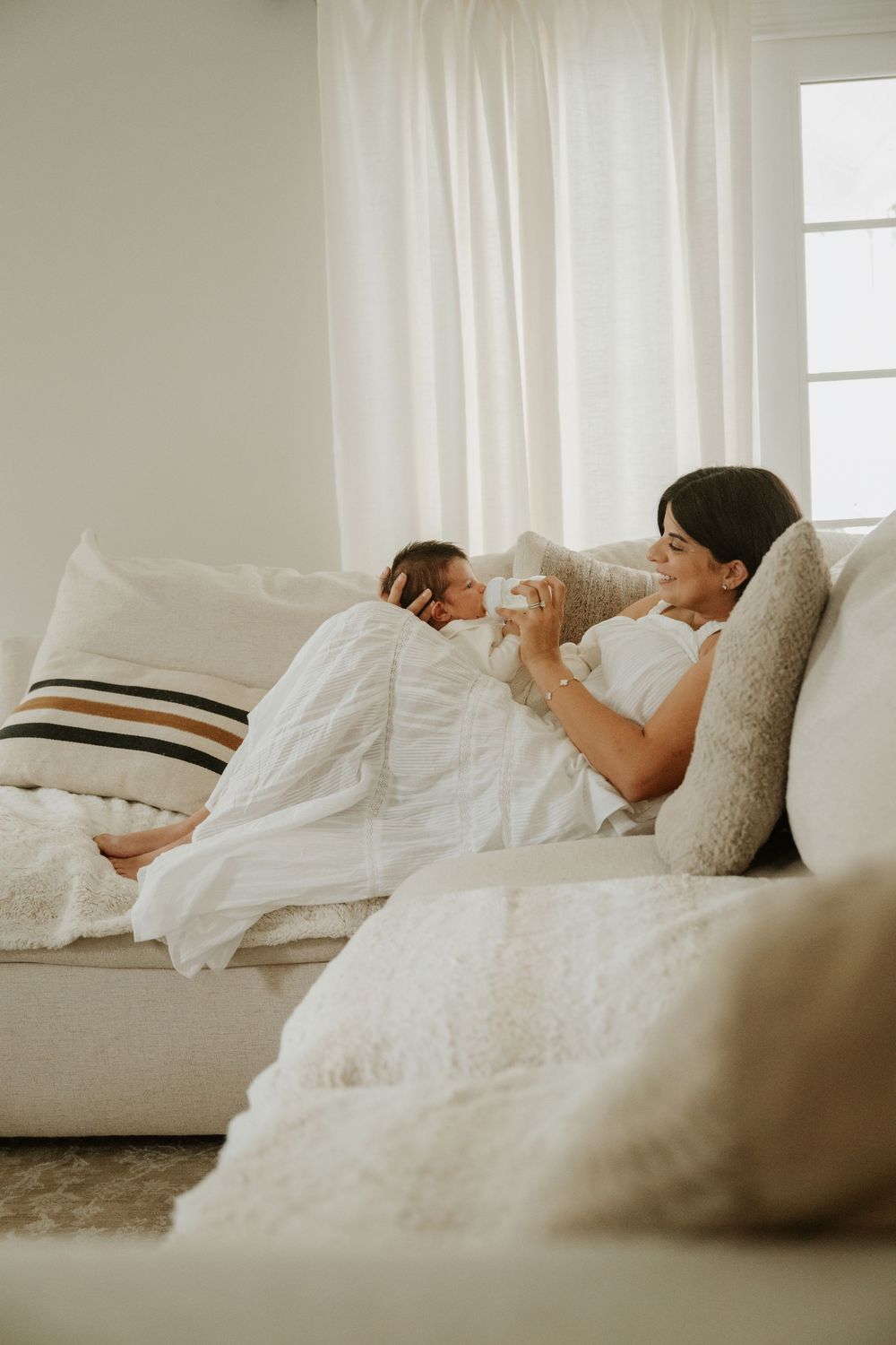Mother bottle-feeding her newborn baby during a relaxed in-home lifestyle newborn session.