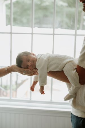 Father holding his newborn baby near a bright window during an in-home lifestyle session.