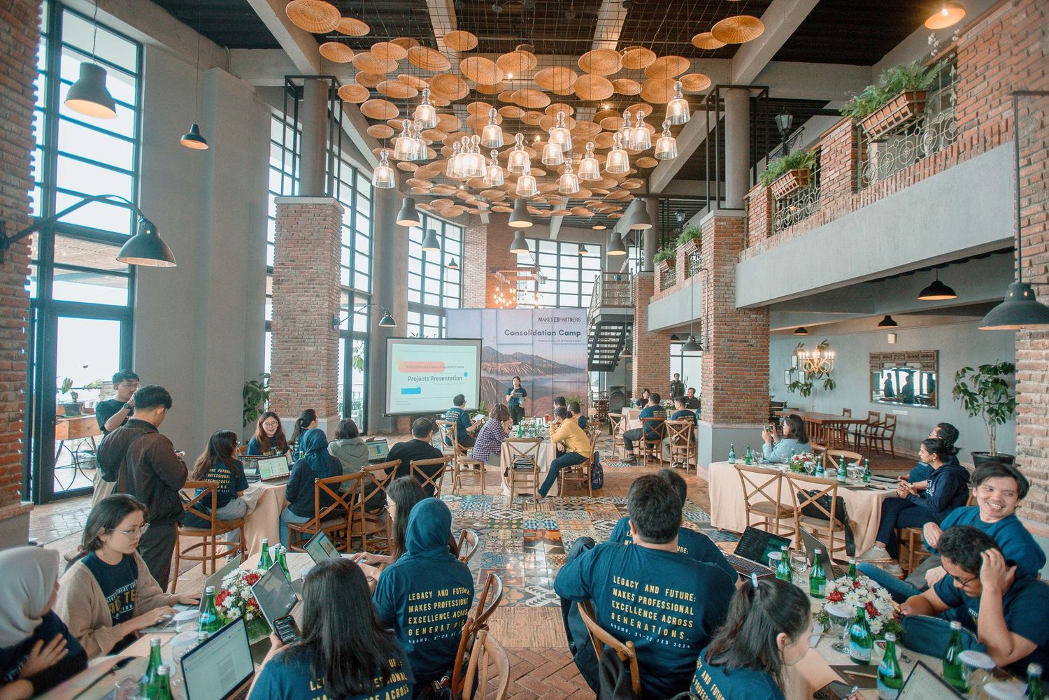 People working on laptops in a modern industrial-style restaurant with brick walls and pendant lights.