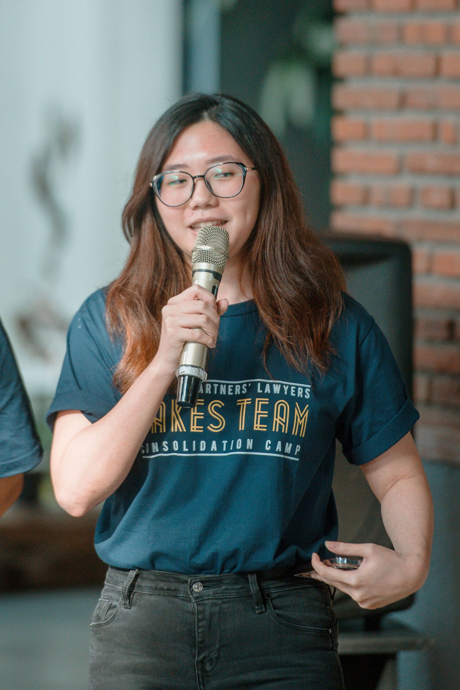 Young woman with glasses speaking into a microphone wearing a navy Lakes Team t-shirt at a consolidation camp event.