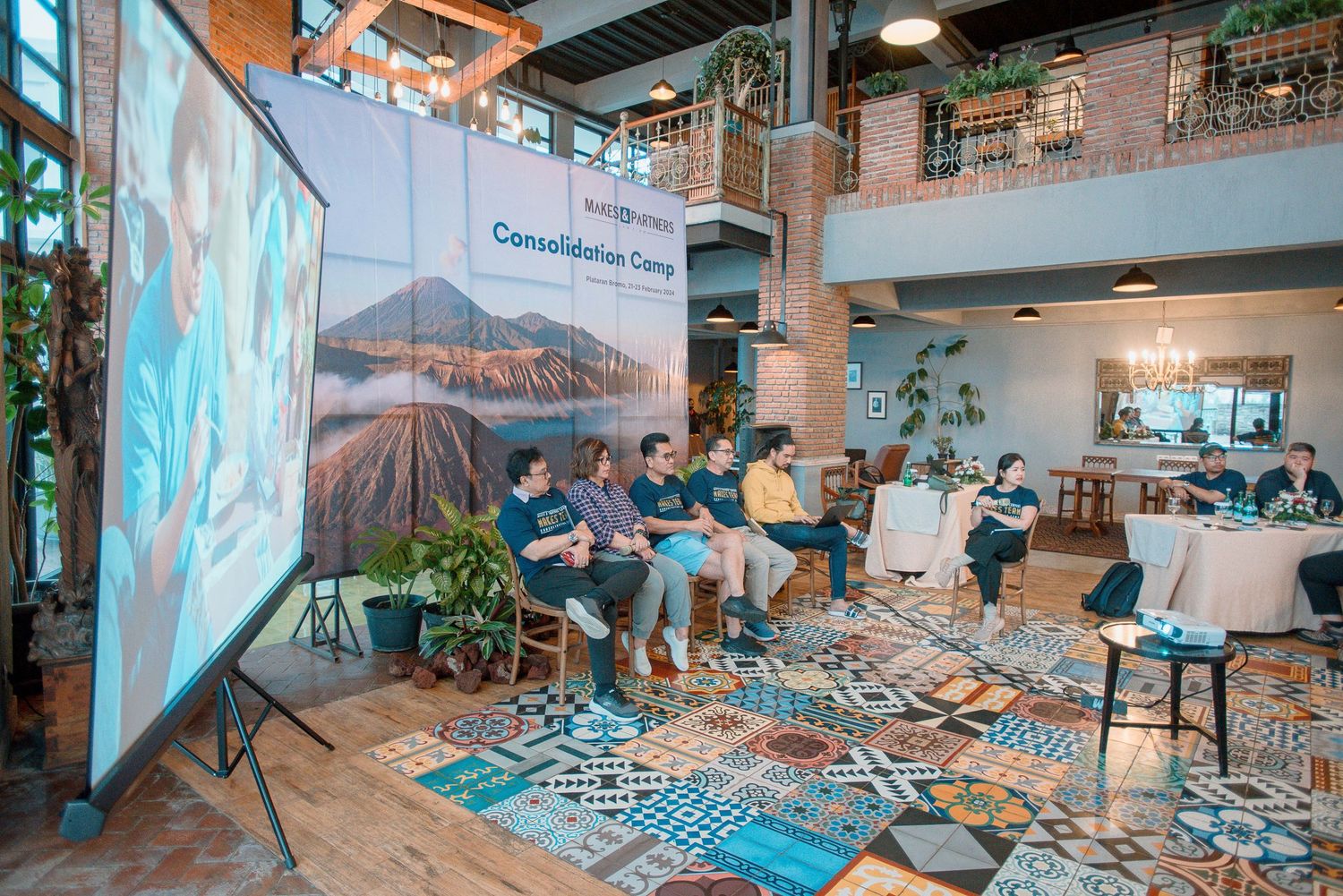 Professionals gathered at a Consolidation Camp event, seated in a modern venue with a large presentation screen.