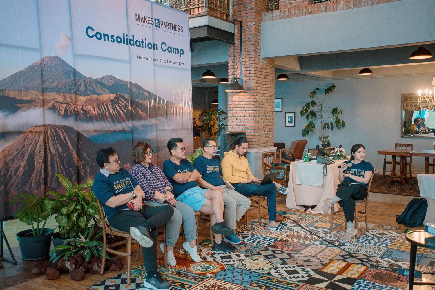 Group of professionals at a Consolidation Camp event seated in front of a Mount Bromo backdrop in a modern venue.