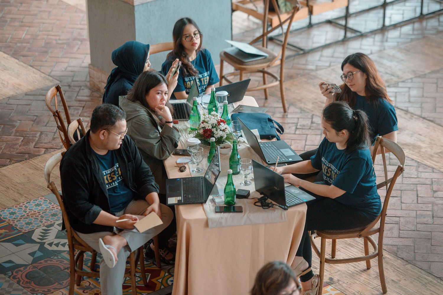 Group of professionals in matching blue shirts collaborating around a table with laptops in a modern workspace.