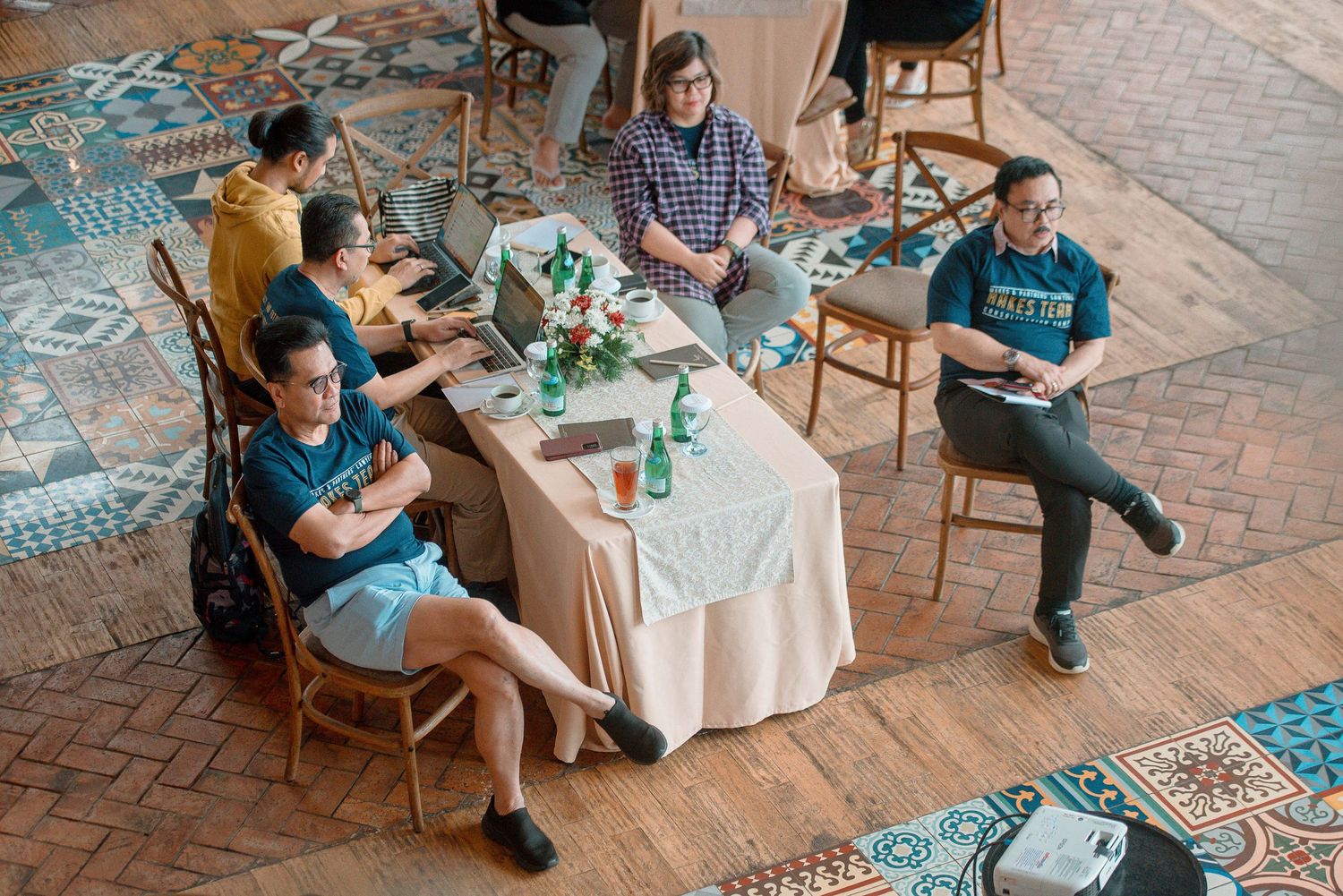 People sitting around a decorated table in a colorful tiled venue during a casual meeting or workshop.