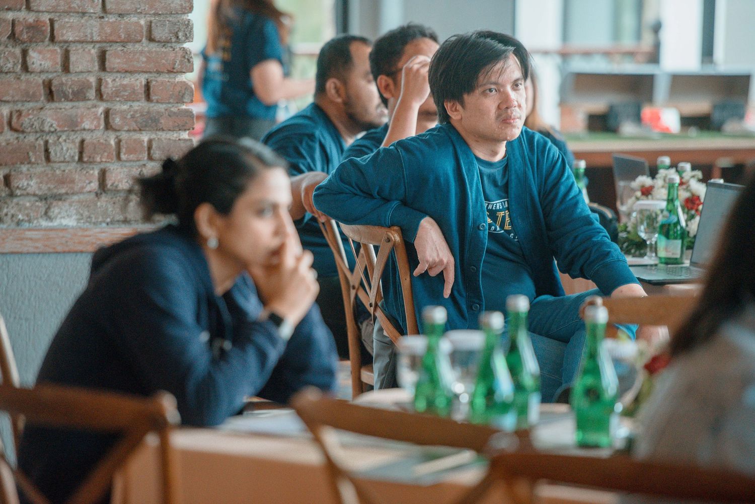 People sitting at tables in a restaurant, attentively listening during a meeting or presentation.