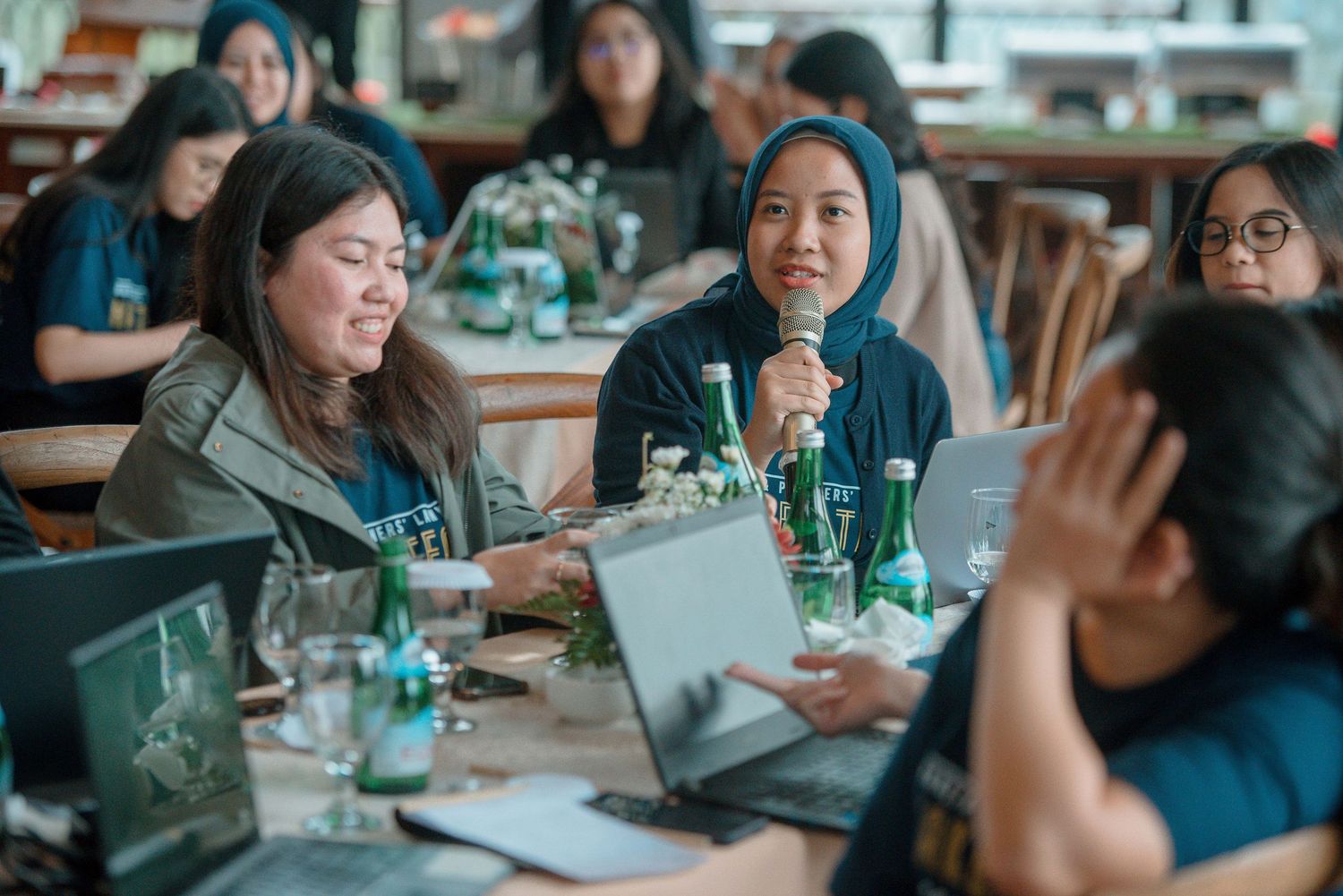 Group of women collaborating at a restaurant table with laptops and green bottles during a business meeting.