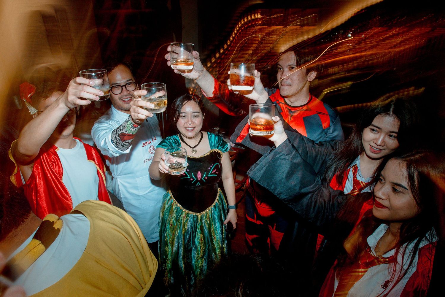 Group of friends in Halloween costumes toasting drinks at a festive party celebration.
