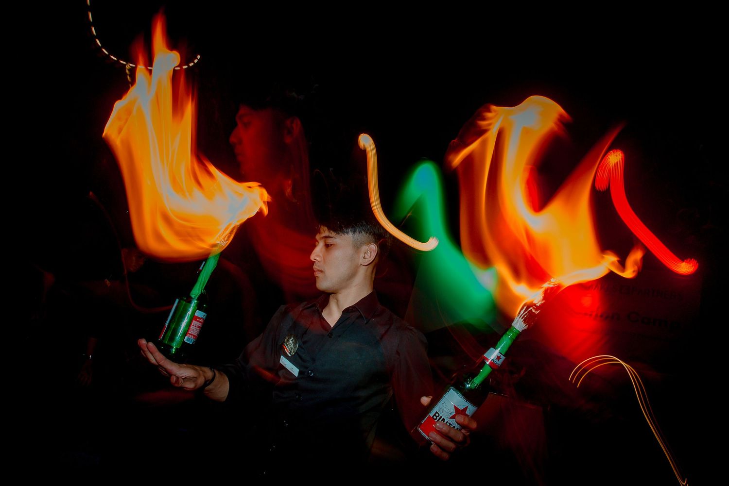 A performer juggles fire torches with colorful light trails in a dark setting.