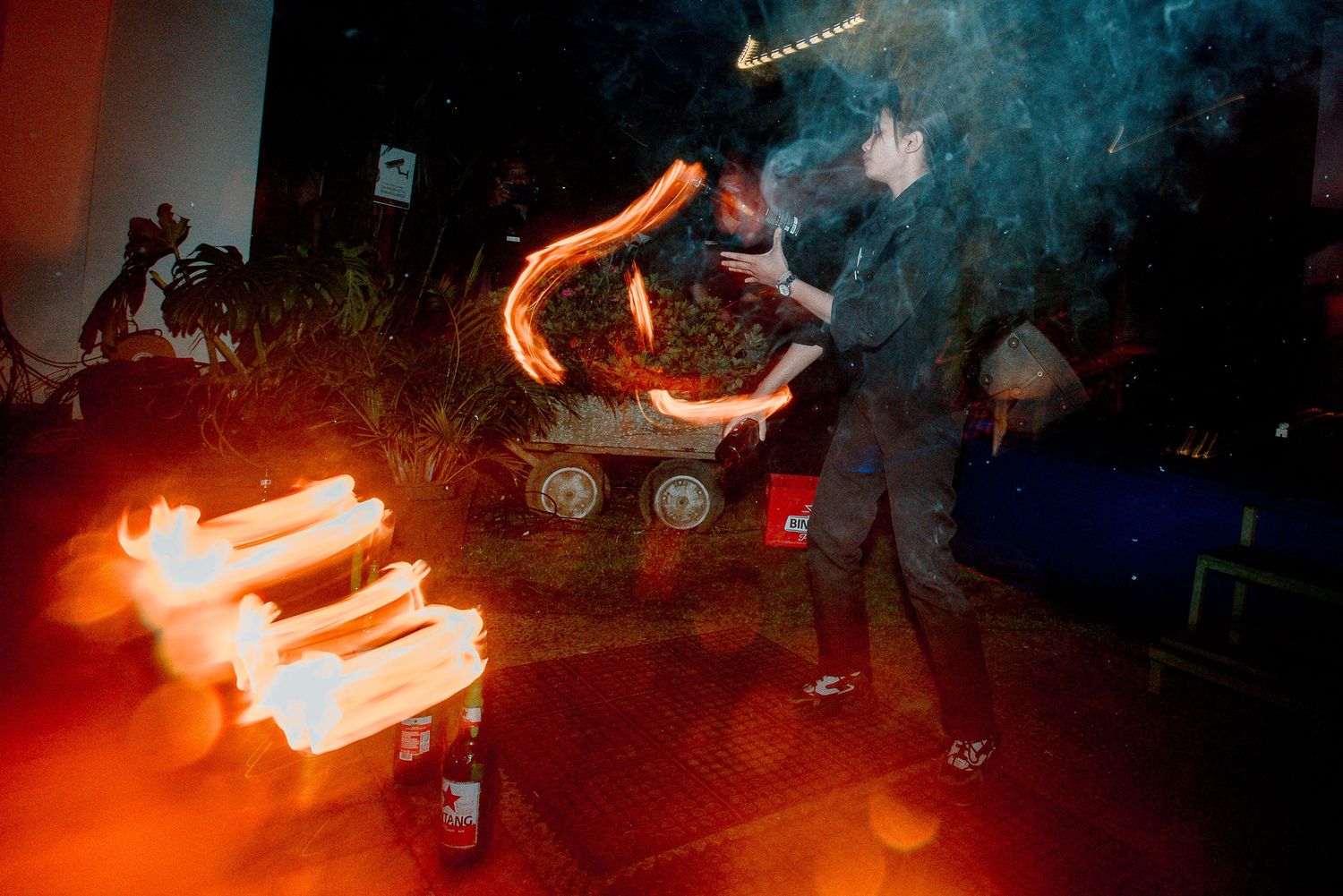 Fire performers create dramatic light trails at a nighttime outdoor event with glowing flames and smoke.