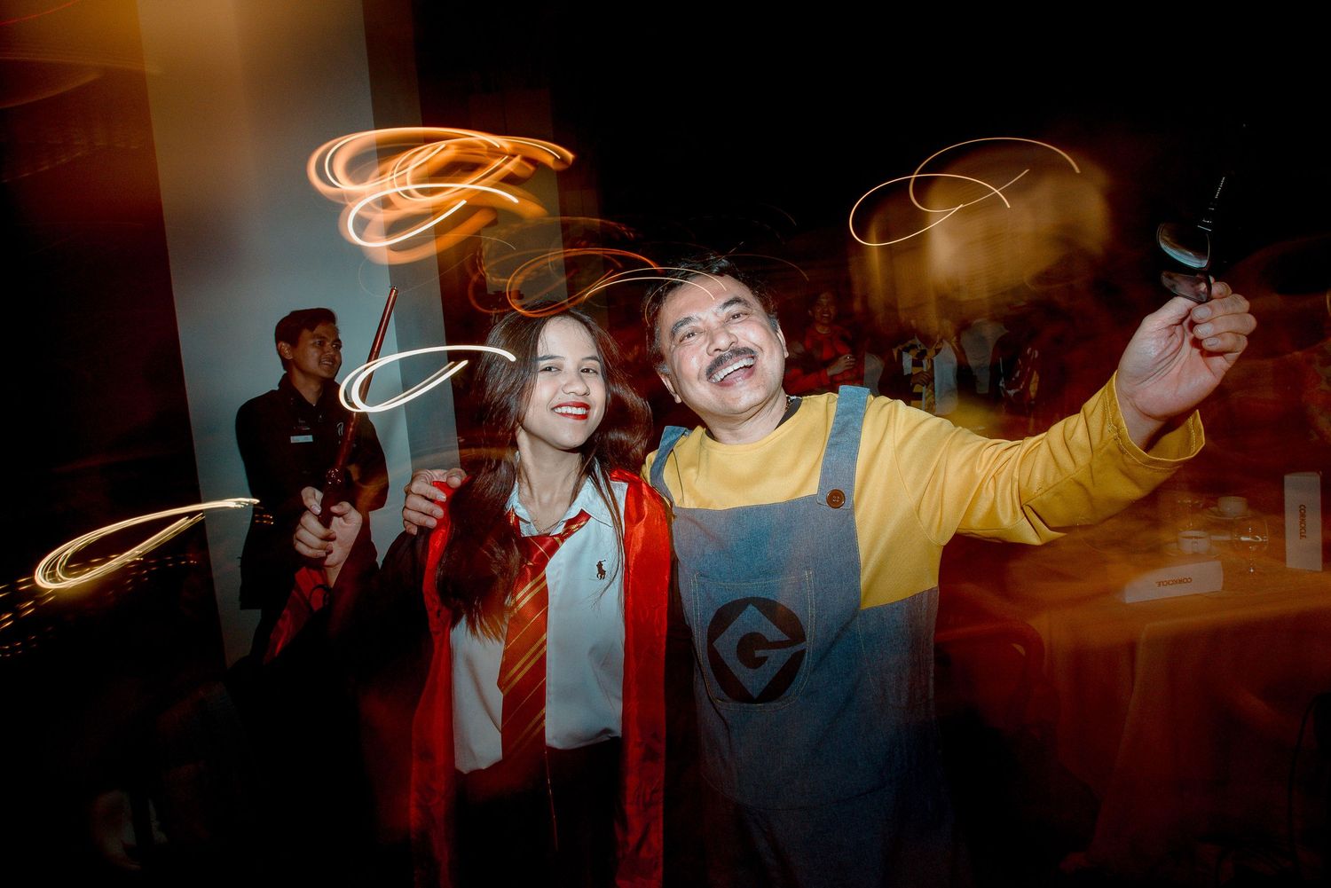 Two friends in costumes wave sparklers creating light trails at a dark party event.