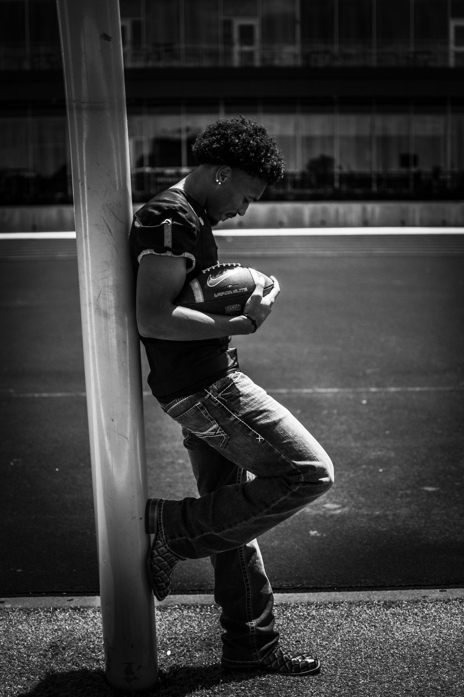 Black and white senior football portrait of a graduate posing with a football on the field