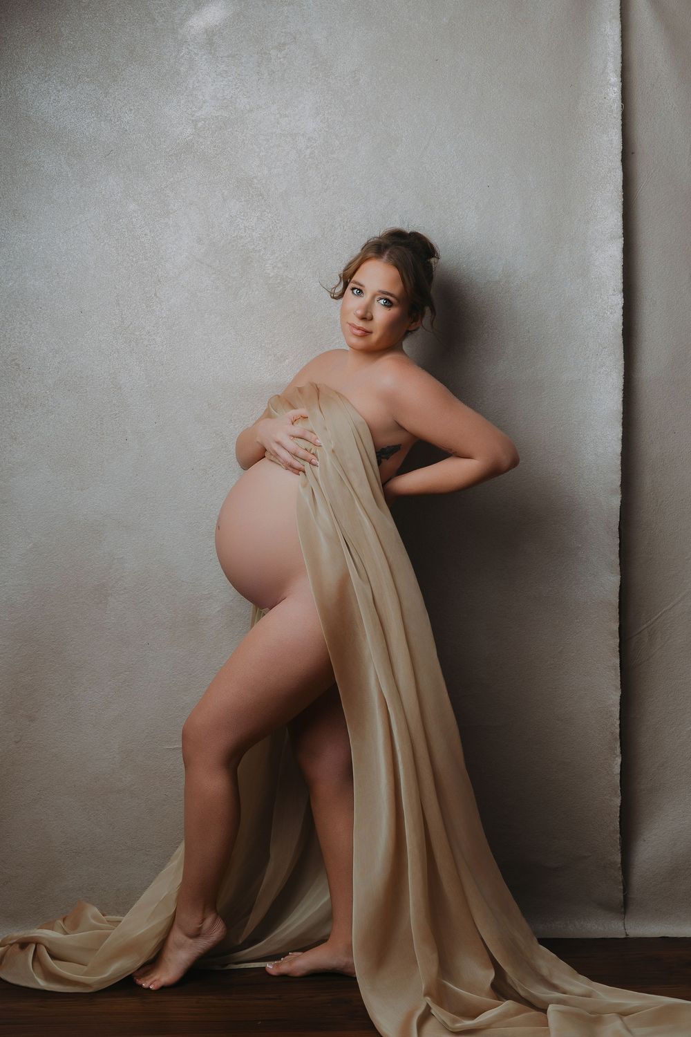 Pregnant woman draped in flowing golden fabric poses gracefully in a studio maternity portrait.