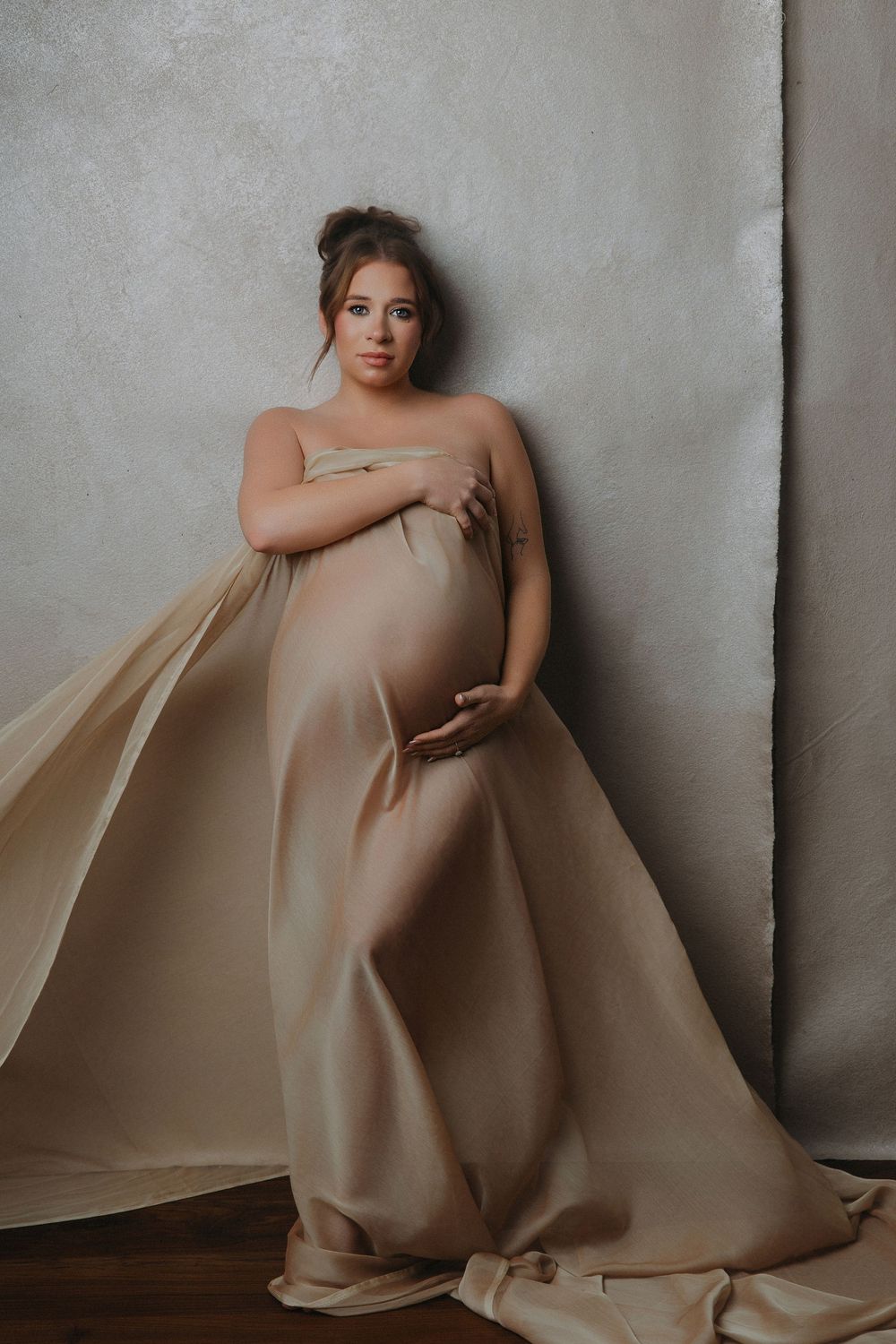 Elegant maternity photo of a pregnant woman wrapped in a luxurious champagne satin fabric.