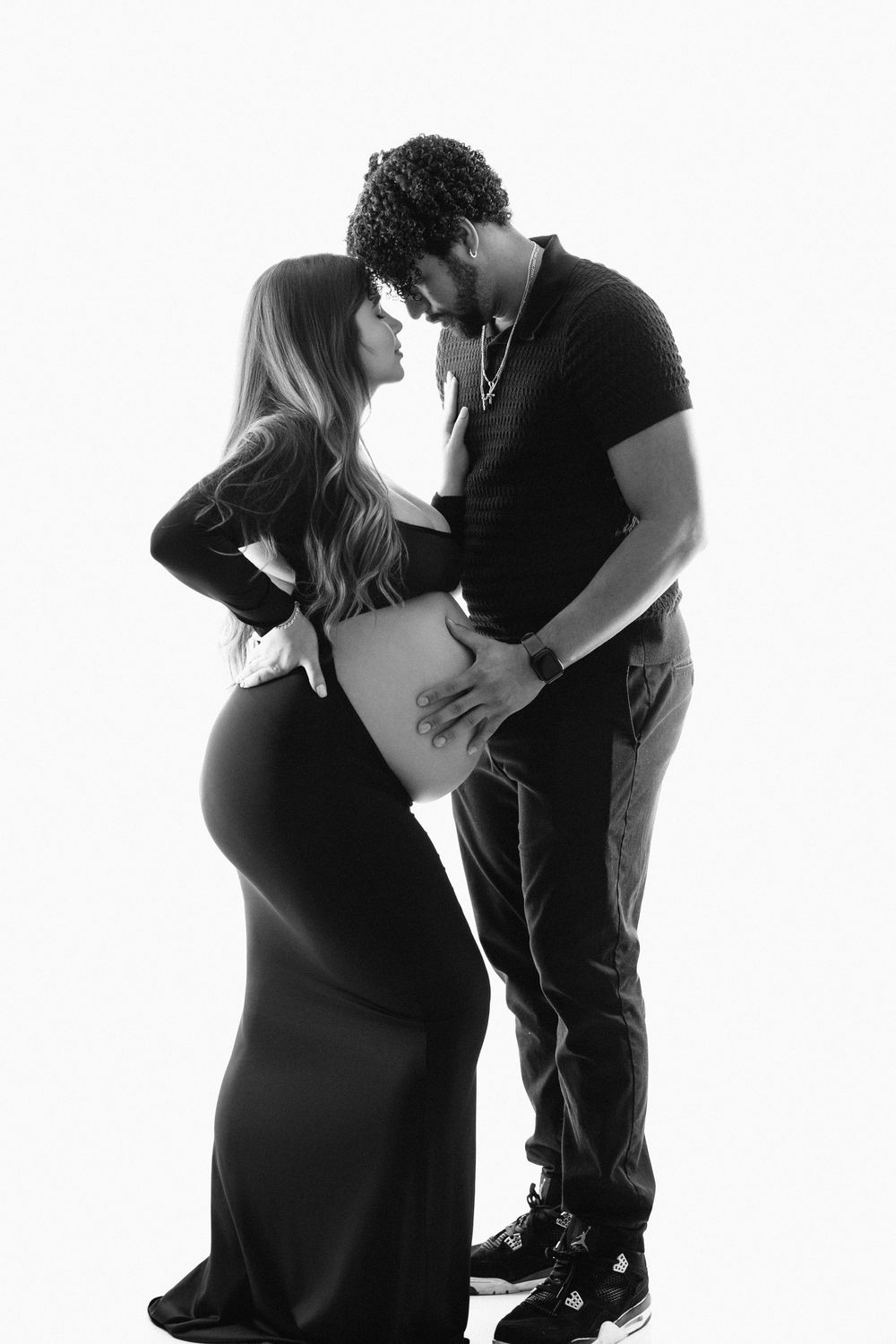 Black and white maternity photo of a couple sharing a tender moment, man cradling pregnant woman's belly.